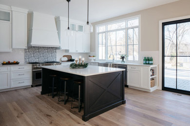 Large arts and crafts u-shaped medium tone wood floor eat-in kitchen photo in Chicago with a farmhouse sink, shaker cabinets, white cabinets, white backsplash, stainless steel appliances, an island and white countertops