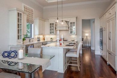 Enclosed kitchen - large traditional u-shaped dark wood floor and brown floor enclosed kitchen idea in Miami with an undermount sink, recessed-panel cabinets, white cabinets, granite countertops, stainless steel appliances, an island, beige backsplash, stone tile backsplash and white countertops
