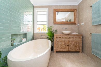 Photo of a medium sized world-inspired ensuite bathroom in Other with freestanding cabinets, light wood cabinets, a freestanding bath, a walk-in shower, green tiles, ceramic tiles, beige walls, porcelain flooring, a vessel sink, wooden worktops, beige floors, an open shower, a wall niche, a single sink and a freestanding vanity unit.