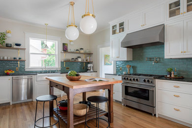 Example of a mid-sized transitional u-shaped medium tone wood floor and brown floor eat-in kitchen design in Portland with a farmhouse sink, shaker cabinets, white cabinets, soapstone countertops, green backsplash, ceramic backsplash, stainless steel appliances, an island and black countertops