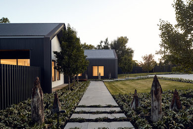 Large contemporary one-storey black house exterior in Melbourne with metal siding, a gable roof and a metal roof.