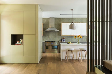 Inspiration for a large contemporary l-shaped open plan kitchen in Austin with an undermount sink, flat-panel cabinets, white cabinets, green splashback, medium hardwood floors, with island, brown floor, white benchtop, quartz benchtops, ceramic splashback and stainless steel appliances.