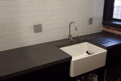 Inspiration for an industrial galley eat-in kitchen remodel in Denver with a farmhouse sink, flat-panel cabinets, black cabinets, concrete countertops, white backsplash, glass tile backsplash and stainless steel appliances