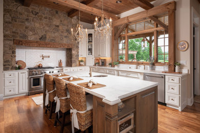 Inspiration for a rustic medium tone wood floor, brown floor and exposed beam eat-in kitchen remodel in Other with an undermount sink, raised-panel cabinets, white cabinets, white backsplash, stainless steel appliances and an island