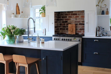 This is an example of a large contemporary single-wall kitchen/diner in West Midlands with a belfast sink, shaker cabinets, blue cabinets, quartz worktops, brick splashback, integrated appliances, medium hardwood flooring, an island and white worktops.