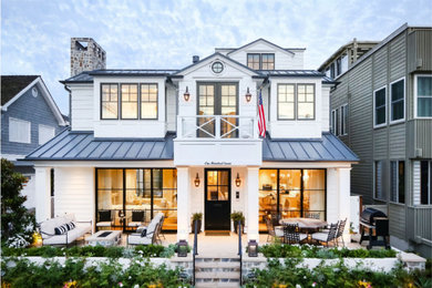 Large beach style two-storey white house exterior in Orange County with vinyl siding, a gable roof and a metal roof.