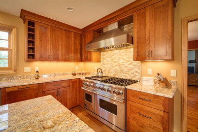 Eat-in kitchen - mid-sized farmhouse u-shaped medium tone wood floor and brown floor eat-in kitchen idea in Milwaukee with a farmhouse sink, granite countertops, beige backsplash, stone tile backsplash, stainless steel appliances, an island, recessed-panel cabinets and medium tone wood cabinets