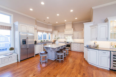 Large elegant u-shaped medium tone wood floor and brown floor open concept kitchen photo in Other with an undermount sink, recessed-panel cabinets, white cabinets, marble countertops, white backsplash, mosaic tile backsplash, stainless steel appliances and an island