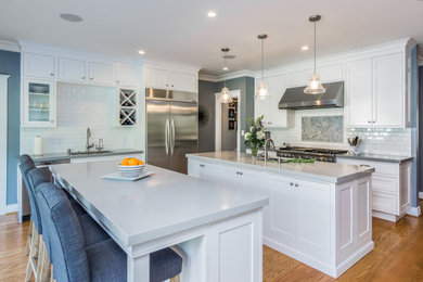 Design ideas for a large transitional kitchen in Los Angeles with an undermount sink, recessed-panel cabinets, white cabinets, quartz benchtops, white splashback, subway tile splashback, stainless steel appliances, medium hardwood floors, multiple islands, brown floor and grey benchtop.