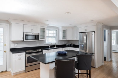 Inspiration for a mid-sized contemporary l-shaped light wood floor and brown floor eat-in kitchen remodel in Raleigh with an undermount sink, white cabinets, stainless steel appliances, an island, black countertops, shaker cabinets and solid surface countertops