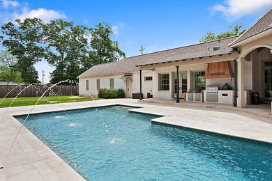 Mid-sized traditional backyard custom-shaped pool in New Orleans with a water feature and natural stone pavers.