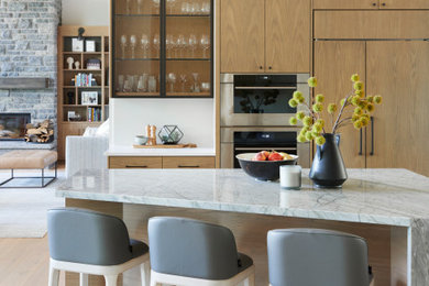 This is an example of a large contemporary u-shaped kitchen/diner in Toronto with flat-panel cabinets, light wood cabinets, engineered stone countertops, white splashback, engineered quartz splashback, integrated appliances, an island and white worktops.