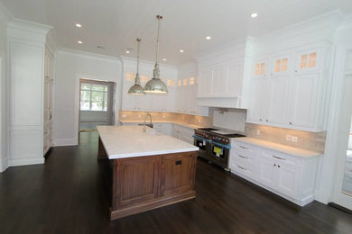 This is an example of a traditional eat-in kitchen in New York with a farmhouse sink, white cabinets, beige splashback, stainless steel appliances, dark hardwood floors and with island.
