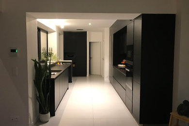 Photo of a mid-sized contemporary single-wall open plan kitchen in Angers with a single-bowl sink, beaded inset cabinets, black cabinets, quartzite benchtops, grey splashback, metal splashback, stainless steel appliances, ceramic floors, no island and beige floor.