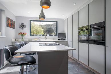 This is an example of a medium sized modern l-shaped kitchen/diner in Other with flat-panel cabinets, grey cabinets, quartz worktops, white splashback, black appliances, an island and white worktops.