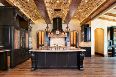 This is an example of a mid-sized mediterranean u-shaped open plan kitchen in Dallas with an undermount sink, raised-panel cabinets, dark wood cabinets, granite benchtops, beige splashback, ceramic splashback, stainless steel appliances, medium hardwood floors and multiple islands.