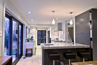 This is an example of a contemporary galley eat-in kitchen in Montreal with an undermount sink, flat-panel cabinets, white cabinets, quartz benchtops, white splashback, subway tile splashback and stainless steel appliances.