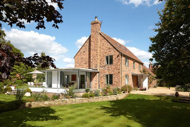 This is an example of an expansive contemporary brick red exterior in Wiltshire with a gable roof.