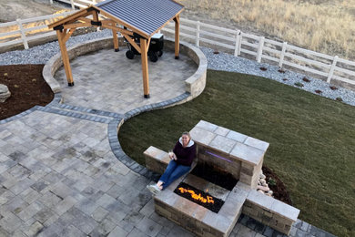 Modelo de patio minimalista grande en patio trasero con chimenea, pérgola y adoquines de hormigón
