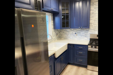 Enclosed kitchen - small traditional l-shaped laminate floor, beige floor and exposed beam enclosed kitchen idea in Los Angeles with a farmhouse sink, raised-panel cabinets, blue cabinets, quartz countertops, multicolored backsplash, glass tile backsplash, stainless steel appliances, a peninsula and white countertops