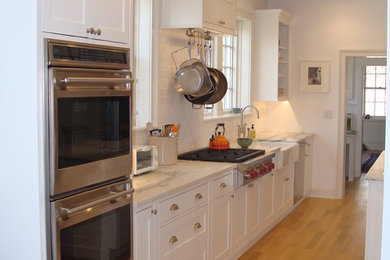 Kitchen pantry - large traditional galley light wood floor kitchen pantry idea in Boston with a farmhouse sink, beaded inset cabinets, white cabinets, marble countertops, white backsplash, subway tile backsplash, stainless steel appliances and an island