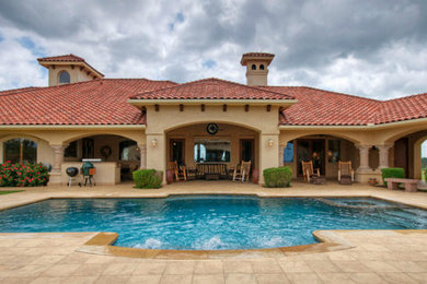 This is an example of a large mediterranean backyard custom-shaped lap pool in Austin with concrete pavers and a hot tub.