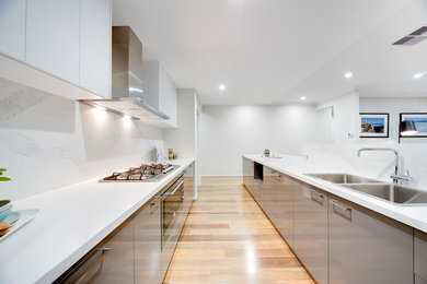 Contemporary l-shaped open plan kitchen in Perth with a double-bowl sink, flat-panel cabinets, grey cabinets, white splashback, stainless steel appliances, light hardwood floors and with island.