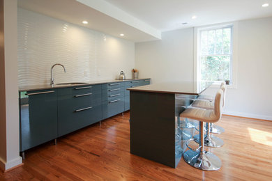 Inspiration for a contemporary medium tone wood floor open concept kitchen remodel in Raleigh with an undermount sink, flat-panel cabinets, blue cabinets, quartz countertops, white backsplash, porcelain backsplash, paneled appliances and an island