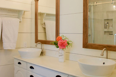 This is an example of a mid-sized country 3/4 bathroom in Vancouver with furniture-like cabinets, a corner shower, white walls, porcelain floors, a vessel sink, brown floor, white cabinets and a sliding shower screen.