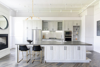 Inspiration for a transitional galley dark wood floor kitchen remodel in Toronto with a farmhouse sink, shaker cabinets, gray cabinets, white backsplash, subway tile backsplash, stainless steel appliances and an island