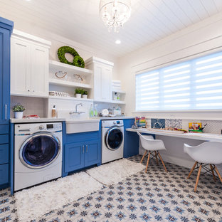 ソルトレイクシティの中サイズのトランジショナルスタイルのおしゃれな家事室 (エプロンフロントシンク、シェーカースタイル扉のキャビネット、青いキャビネット、クオーツストーンカウンター、セラミックタイルの床、左右配置の洗濯機・乾燥機、白い壁、マルチカラーの床) の写真