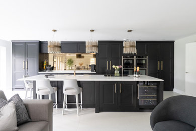 Design ideas for a large traditional cream and black single-wall kitchen/diner in Sussex with a built-in sink, shaker cabinets, black cabinets, quartz worktops, metallic splashback, mirror splashback, black appliances, porcelain flooring, an island, white floors, white worktops and feature lighting.