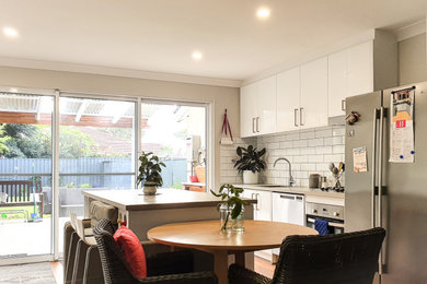 This is an example of a mid-sized country galley open plan kitchen in Perth with a single-bowl sink, shaker cabinets, white cabinets, laminate benchtops, white splashback, ceramic splashback, stainless steel appliances, laminate floors, with island and grey benchtop.