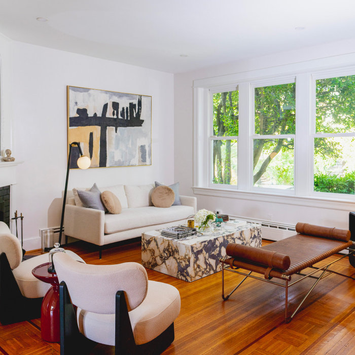 This inviting living room features a harmonious blend of modern elegance and timeless comfort. At the heart of the space, a minimalist beige sofa is paired with two cream lounge chairs, creating a coz