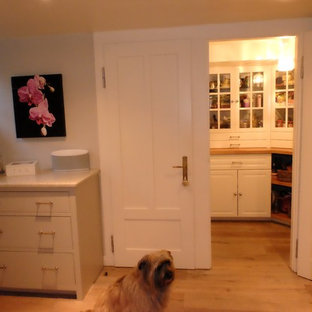 Mid-sized farmhouse kitchen pantry remodeling - Example of a mid-sized farmhouse single-wall medium tone wood floor and brown floor kitchen pantry design in Frankfurt with raised-panel cabinets, white cabinets, wood countertops, an island, a farmhouse sink, gray backsplash, stone slab backsplash and stainless steel appliances