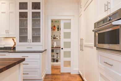 Eat-in kitchen - large u-shaped medium tone wood floor eat-in kitchen idea in Portland Maine with shaker cabinets, white cabinets, wood countertops, stainless steel appliances and an island