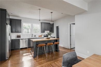 Mid-sized modern l-shaped eat-in kitchen in Indianapolis with an undermount sink, recessed-panel cabinets, grey cabinets, wood benchtops, white splashback, subway tile splashback, stainless steel appliances, medium hardwood floors, with island and brown floor.