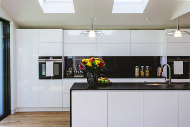 Inspiration for a large contemporary single-wall open plan kitchen in London with flat-panel cabinets, white cabinets, black splashback, medium hardwood floors and with island.