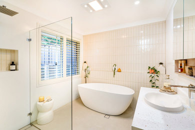 Photo of a large master bathroom in Sydney with flat-panel cabinets, medium wood cabinets, a freestanding tub, a corner shower, white tile, subway tile, white walls, ceramic floors, engineered quartz benchtops, beige floor, an open shower, white benchtops, a niche, a single vanity and a floating vanity.