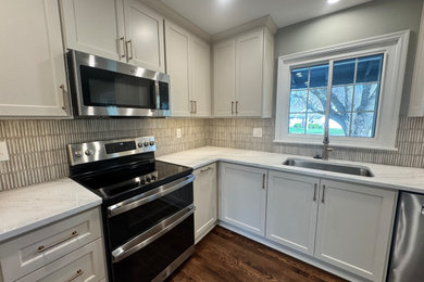Example of a mid-sized minimalist u-shaped medium tone wood floor and brown floor eat-in kitchen design in Kansas City with an undermount sink, shaker cabinets, white cabinets, quartz countertops, white backsplash, ceramic backsplash, stainless steel appliances, no island and white countertops