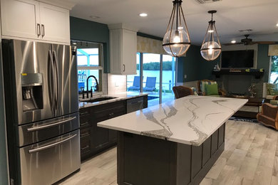 This is an example of a mid-sized beach style u-shaped kitchen in Miami with shaker cabinets, white splashback, subway tile splashback, stainless steel appliances, porcelain floors, an undermount sink, quartz benchtops, with island and white benchtop.
