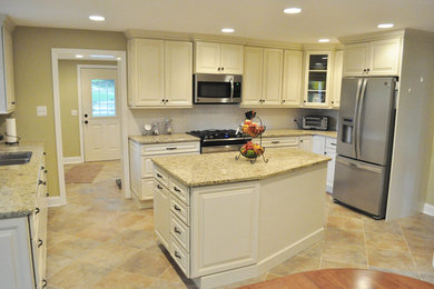 Photo of a large traditional u-shaped eat-in kitchen in Philadelphia with an undermount sink, raised-panel cabinets, beige cabinets, granite benchtops, white splashback, stainless steel appliances, porcelain floors, with island and brown floor.