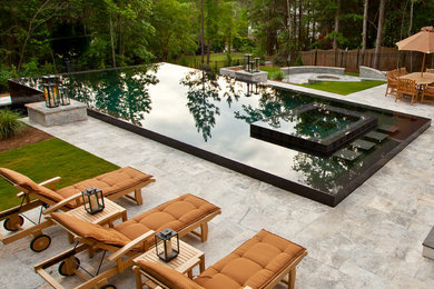 Example of a large trendy backyard stone and rectangular infinity hot tub design in Other