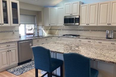 Example of a mid-sized farmhouse l-shaped light wood floor, beige floor and vaulted ceiling eat-in kitchen design in Seattle with an undermount sink, beaded inset cabinets, beige cabinets, granite countertops, beige backsplash, ceramic backsplash, stainless steel appliances, an island and beige countertops