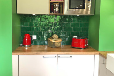 Exemple d'une petite cuisine ouverte linéaire et blanche et bois exotique avec un évier 1 bac, un placard à porte plane, un plan de travail en bois, une crédence verte et parquet clair.