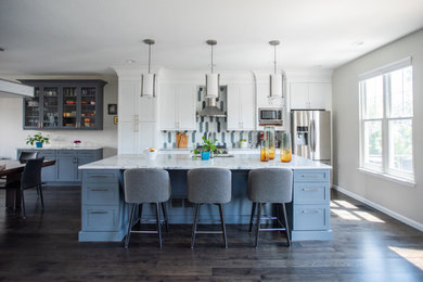 Example of a mid-sized transitional single-wall dark wood floor and gray floor open concept kitchen design in Denver with an undermount sink, shaker cabinets, white cabinets, quartz countertops, gray backsplash, glass tile backsplash, stainless steel appliances, an island and white countertops