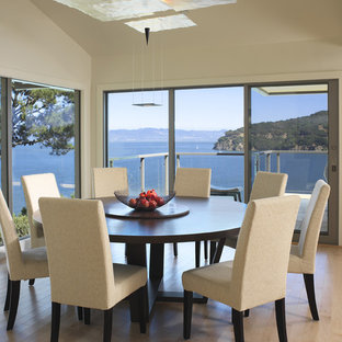 Idée de décoration pour une salle à manger ouverte sur la cuisine design de taille moyenne avec un mur blanc, un sol en bois clair, une cheminée double-face, un sol beige et un manteau de cheminée en métal.
