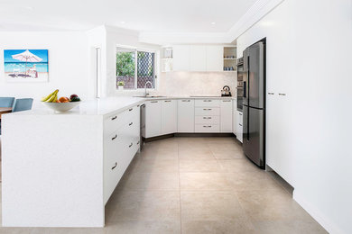 Photo of a large modern u-shaped separate kitchen in Sunshine Coast with a drop-in sink, flat-panel cabinets, white cabinets, multi-coloured splashback, stainless steel appliances, ceramic floors, beige floor and white benchtop.