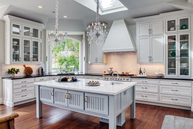 Example of a transitional u-shaped medium tone wood floor and brown floor eat-in kitchen design in San Francisco with an undermount sink, shaker cabinets, white cabinets, white backsplash, subway tile backsplash, white appliances, an island and white countertops