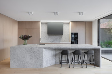 Modern galley kitchen in Melbourne with a submerged sink, flat-panel cabinets, light wood cabinets, light hardwood flooring, an island, beige floors and grey worktops.